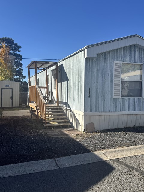 A wooden building with a porch and a staircase leading to a door.